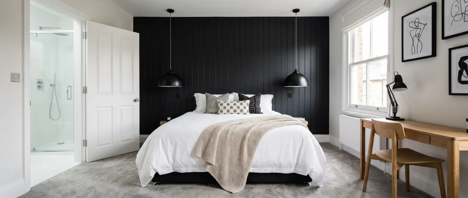 En-suite bedroom with a black panelled feature wall, pendant lights, a double bed and a desk by the window