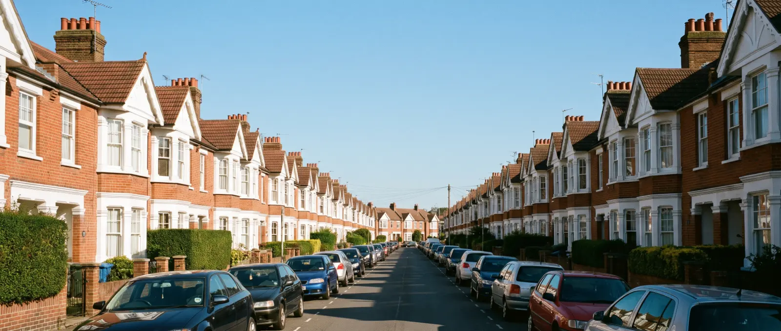 A long late-Victorian terraced street of red-brick houses with white gabled bays, cars parked along both sides